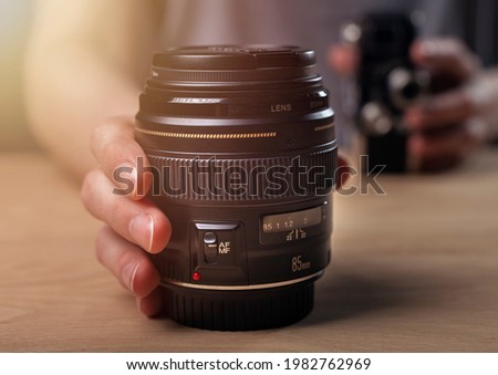 Photographer showing camera lens, blurred vintage old one and modern 85 mm portrait lens. Royalty-Free Stock Photo #1982762969