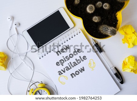 Notebook with NEW PODCAST EPISODE available now lettering. Headphones and mobile phone. Top view layout. Workplace. Audiobooks Royalty-Free Stock Photo #1982764253