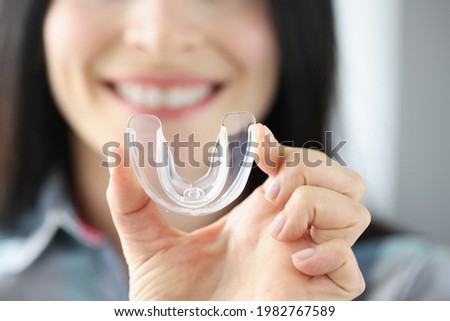 Smiling woman holds transparent plastic mouth guard in her hand Royalty-Free Stock Photo #1982767589