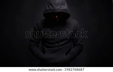 Man in Black Hood in dark studio. Boy in a hooded sweatshirt. Male portrait