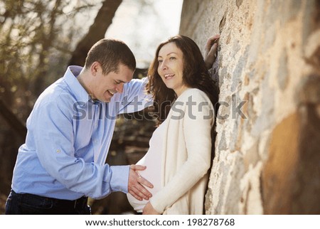 Happy young pregnant couple hugging in nature