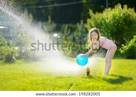 Little girl running though a sprinkler in a backyard
