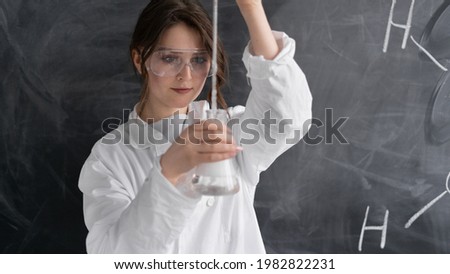 Closeup porter woman chemistry teacher stands in a white coat on the background of a chalk board. He holds a test tube in his hands and conducts an experiment. Back to school concept. Copy space.