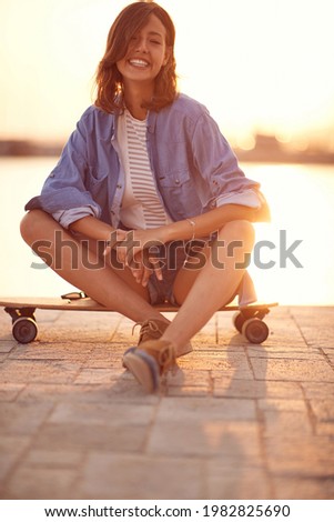 Happy attractive woman posing with the skateboard on a sunny day