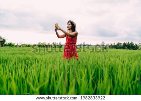 Beautiful female tourist photographing nature environment while visiting Indonesian rice fields at Ubud using modern smartphone technology for memorise moment, millennial blogger shooting vlog