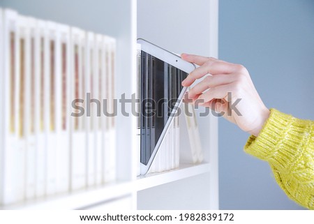 Close up of a woman taking digital tablet from bookshelf Royalty-Free Stock Photo #1982839172
