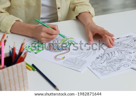 Young woman coloring antistress page at table indoors, closeup