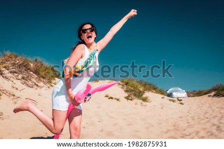 Brunette teen girl on vacation on beach. Young woman having fun playing with inflatable pink hare outdoor in the summer. Woman playing superhero
