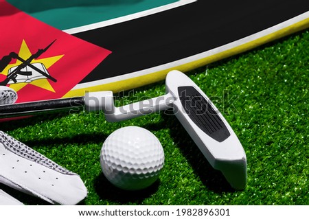Golf ball and club with flag of Mozambique on green grass. Golf championship in Mozambique