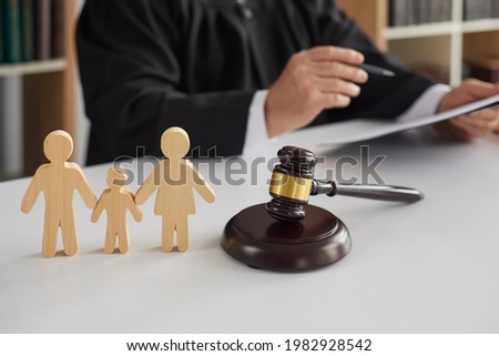 Close up of wooden figurines of family with child and gavel on background of judge conducting divorce process. Concept of alimony, family law and child custody. Royalty-Free Stock Photo #1982928542