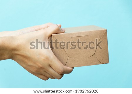 Woman hand hold the brown corrugated box on blue  wall background with copy space