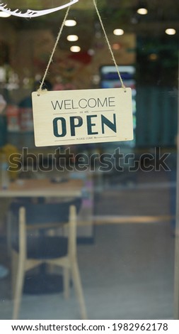 Open and closed flip sign in front of coffee shop and restaurant glass door. Wooden sign with wording of place's status. Welcome, we're open banner.