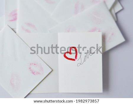 Open empty card with heart shape red lipstick and love word, in the background of white envelopes with lipstick kiss masks. 