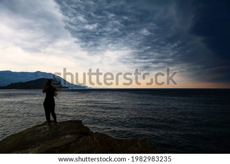 Girl standing on the seaside in the stormy weather and taking a pictures by smartphone . Altocumulus dark clouds over the sea