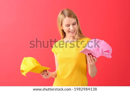 Beautiful young woman with stylish caps on color background