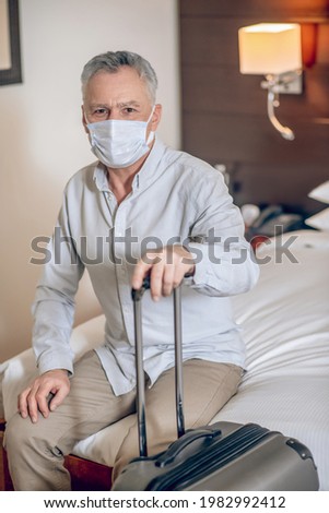 In the hotel room. Gray-haired mid-aged man with a protective mask in a hotel room