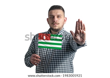 White guy holding a flag of Abkhazia and with a serious face shows a hand stop sign isolated on a white background.