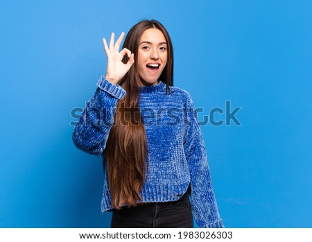 young pretty casual woman feeling successful and satisfied, smiling with mouth wide open, making okay sign with hand