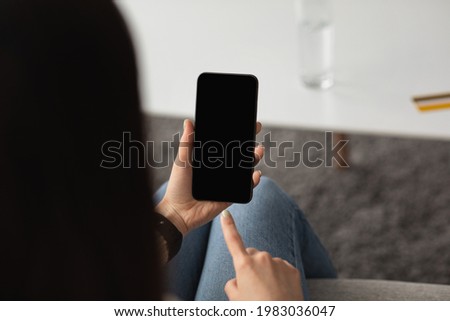 Technology for communication, surfing on internet, chat in social networks and be safe at home. Young lady holds phone with empty screen, in living room interior with table with credit card and glass