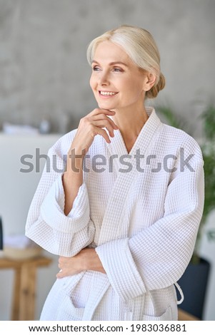 Happy smiling gorgeous senior aged woman in bathrobe at spa hotel looking away. Advertising of bodycare spa procedures recreation rejuvenation skin care salon concept. Vertical shot. Royalty-Free Stock Photo #1983036881