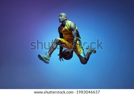 In motion. Portrait of athletic african-american male basketball player training isolated in neon light on blue background. Concept of health, professional sport, hobby. Passionate, fashionable Royalty-Free Stock Photo #1983046637