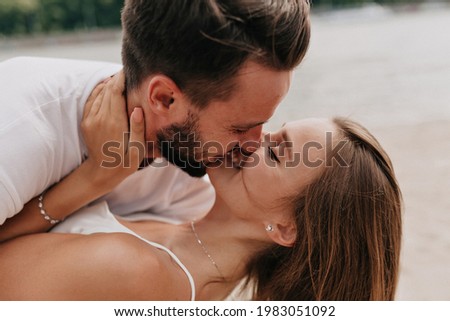 Close up outdoor portrait of two young people are kissing and hugging while walking on the beach in summer day. High quality photo