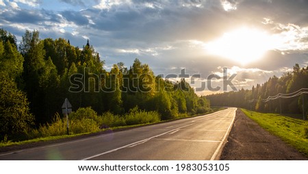 Country road with markings in the middle of the forest. Path and forward movement in the sun. Beautiful, green forest in the spring at sunset. Concept for success in the future goal and passing time Royalty-Free Stock Photo #1983053105