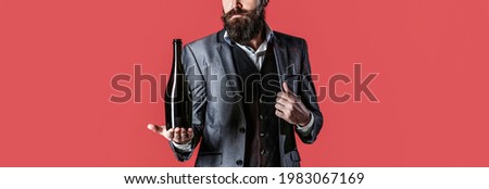 The person holds a red wine bottle in a hand. Man holding bottle with champagne, wine. Bearded man with a bottle champagne of and glass.
