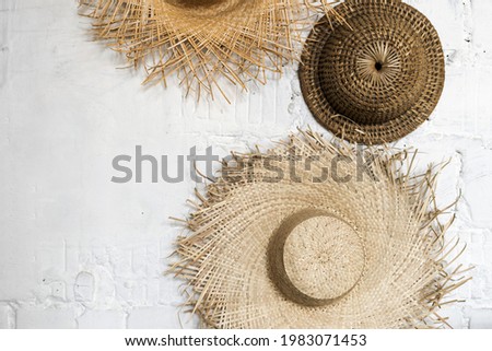 Minimalist picture of straw sun hats on white concrete wall indoors, top view. Summer background with copy space for text. Creative design concept