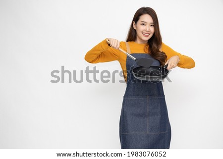 Young Asian woman housewife wearing kitchen apron cooking and holding pan and spatula isolated on white background Royalty-Free Stock Photo #1983076052