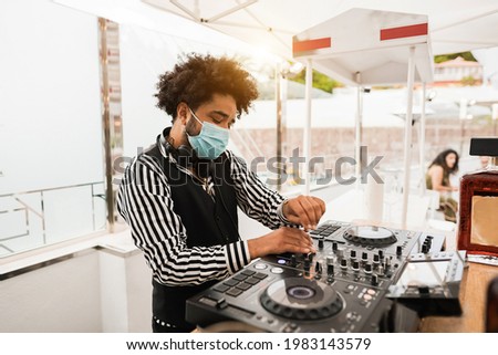 African dj playing music at cocktail bar outdoor while wearing face safety mask - Entertainment, social distance and party concept - Focus on face