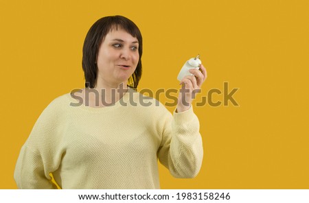 a woman in a sweater looks in surprise at an alarm clock in an outstretched hand on a yellow background