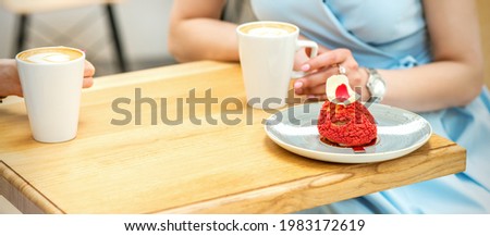 Two young girlfriends drinking coffee with pieces of cake sitting at the table in a cafe outdoors