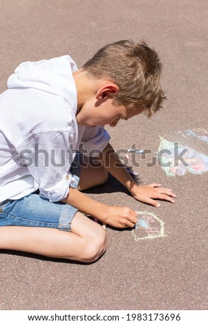 Little boy is drawing with a chalk on a pavement