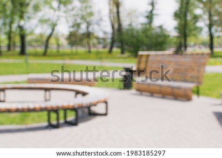 A blurry image of a city park in summer with wooden decorative benches