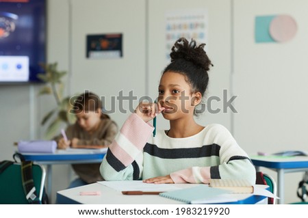 Portrait of teenage African-American girl sitting at desk in school classroom, copy space Royalty-Free Stock Photo #1983219920