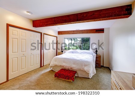 Bedroom in white color. Room has bright brown ceiling beams.