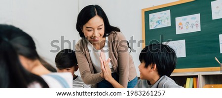 Young Asian teacher giving boy high five in school, success, achievement, happiness. Asia school boy with young woman in class. Royalty-Free Stock Photo #1983261257