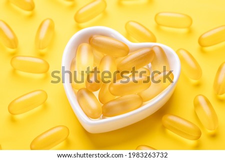 Vitamin D and Omega 3 fish oil capsules supplement in a heart-shaped plate on yellow background. Concept of healthcare. Top view - Image