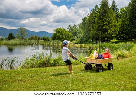 Small kid pulling a cart with an older child. Family fun, summer vacation. Copy space for your text