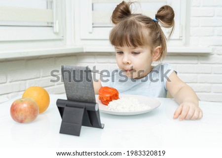 Little girl is having breakfast while watching the movie on the tablet