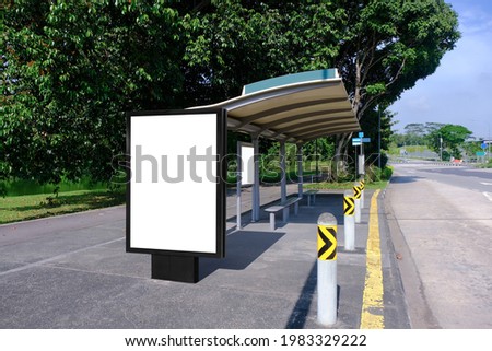 Blank advertising poster banner mockup at empty bus stop shelter by main road, greenery behind; out-of-home OOH vertical billboard media display space. Perspective angle Royalty-Free Stock Photo #1983329222