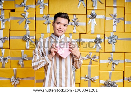 Best prices for gifts. Handsome Asian Man in studio room full of packed gifts, many holiday packages. Holidays filled with fun.