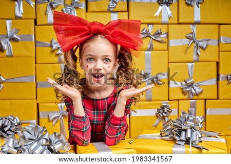 Joyful child girl in checkered wear stand among gifts presents. Little caucasian kid looking inspired, celebrating