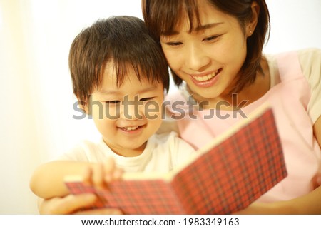 Image of a boy reading a picture book and a nursery teacher 
