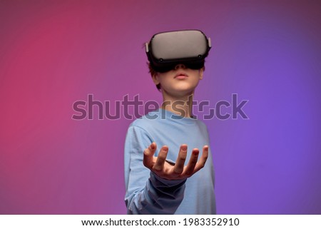 teen boy trying VR headset and exploring another world on the colorful background. boy using VR headset, spreading arms, looking at side. Portrait. Boy Playing virtual game. focus on hands