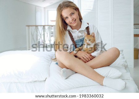 The girl is resting on the bed with her ginger kitten. A child with an animal. High quality photo.