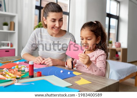 family, art and craft concept - mother spending time with her little daughter with glue making applique of color paper at home Royalty-Free Stock Photo #1983400589