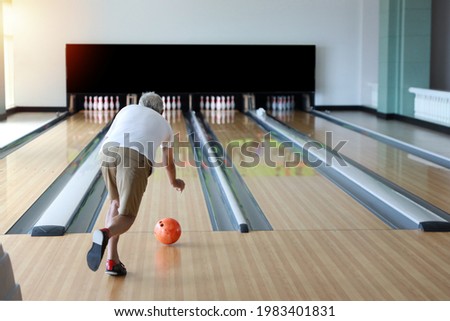 rear view older caucasian men, white beard and white hair in white and blue shirt playing bowling in sport club