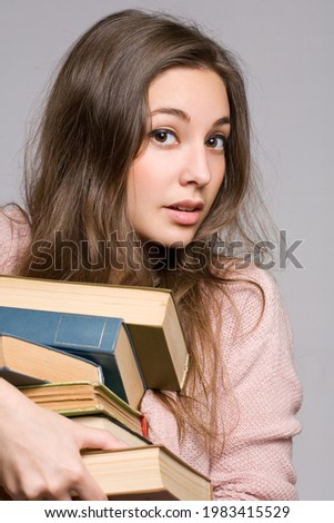Beautiful young brunette student woman trying to hold a large pile of books.